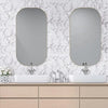 A bathroom vanity featuring two oval mirrors above white sinks on a light wood countertop with marble-patterned walls.