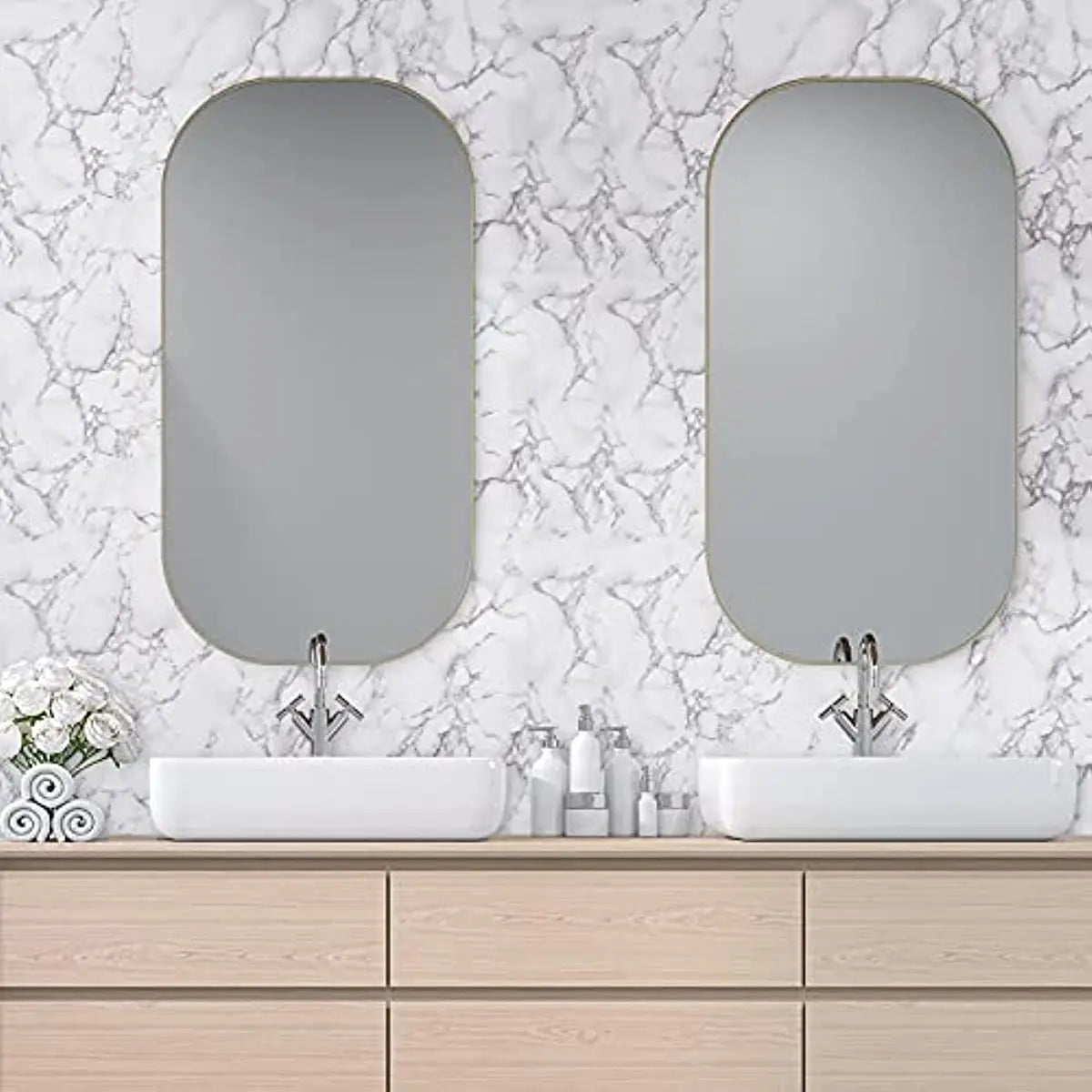 A bathroom vanity featuring two oval mirrors above white sinks on a light wood countertop with marble-patterned walls.