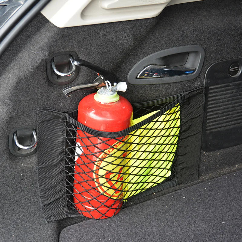 A red bottle is stored in an elastic mesh pocket within a black car seat back organizer.