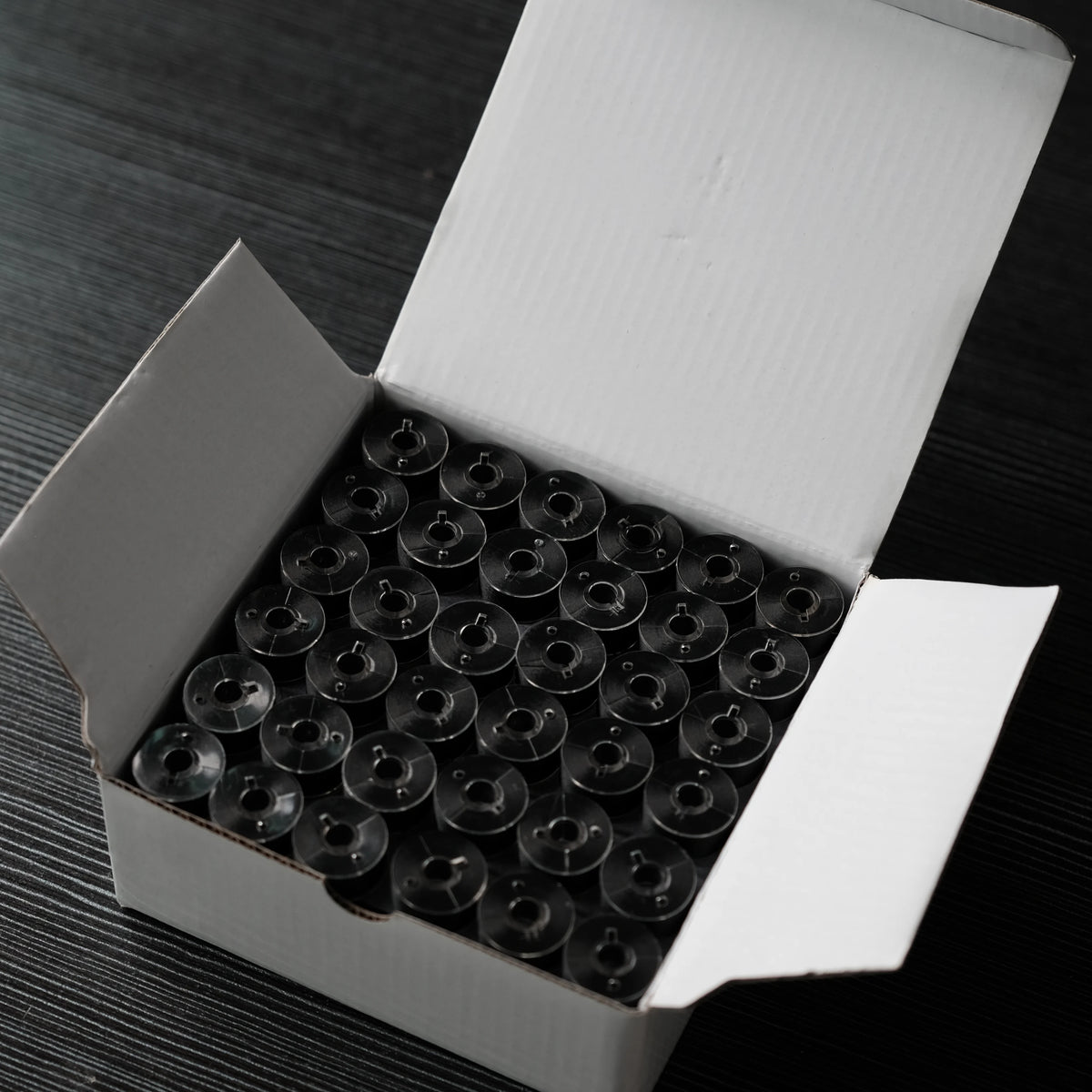A white box containing numerous prewound bobbins with 60wt polyester thread for home embroidery machines.