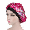 A woman wearing a vibrant pink satin hair bonnet with floral patterns and a black elastic band.