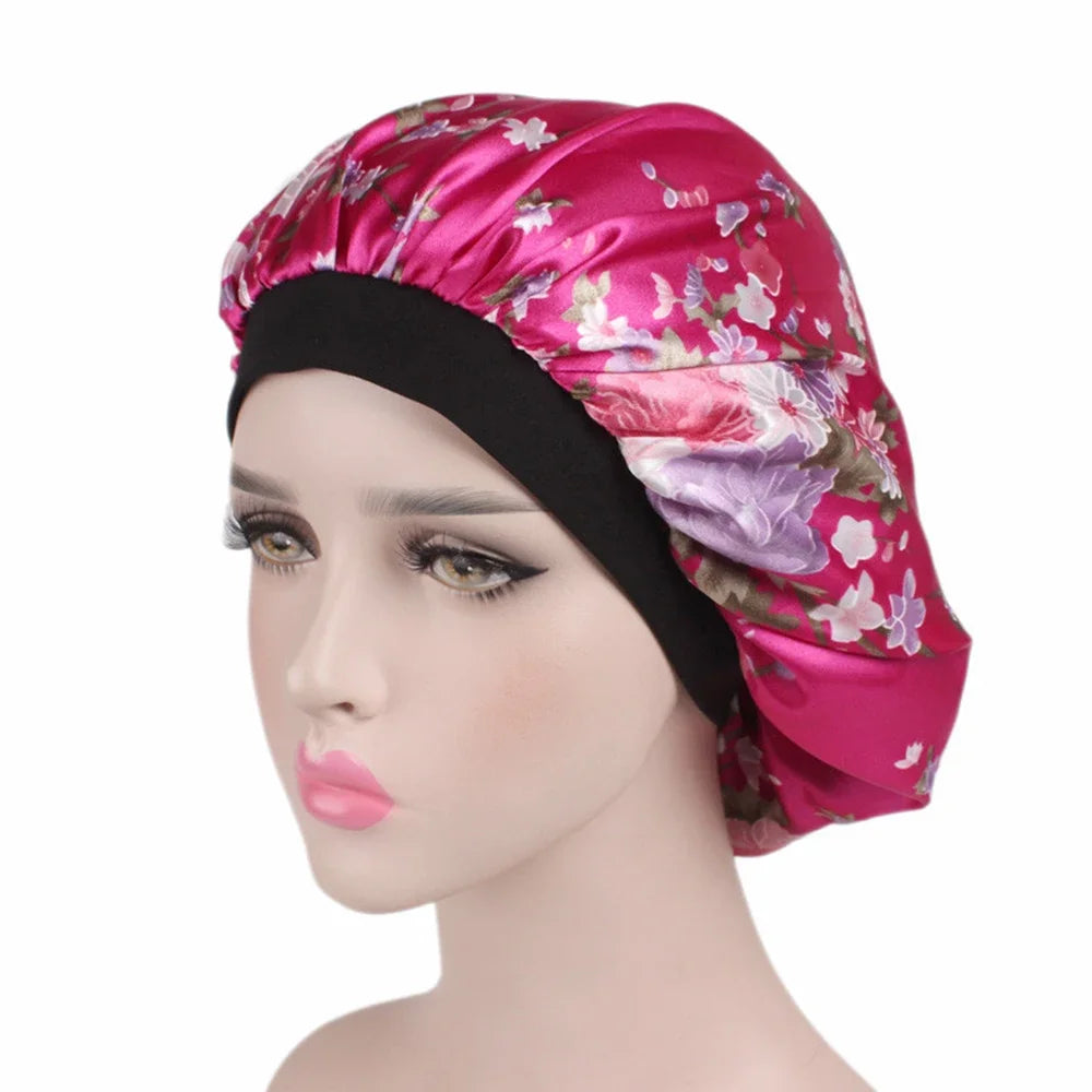 A woman wearing a vibrant pink satin hair bonnet with floral patterns and a black elastic band.
