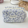 A quilted floral makeup bag with a white background and blue and purple flowers, featuring a zipper closure.