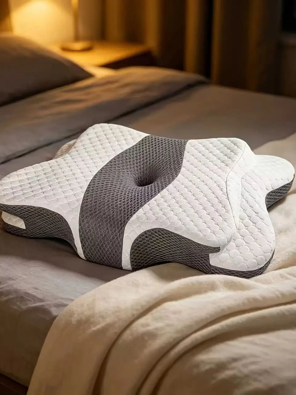 A white and gray ergonomic butterfly memory foam pillow resting on a bed with soft bedding.