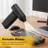 A black portable blower is shown next to a laptop and a textured cleaning brush on a wooden desk.