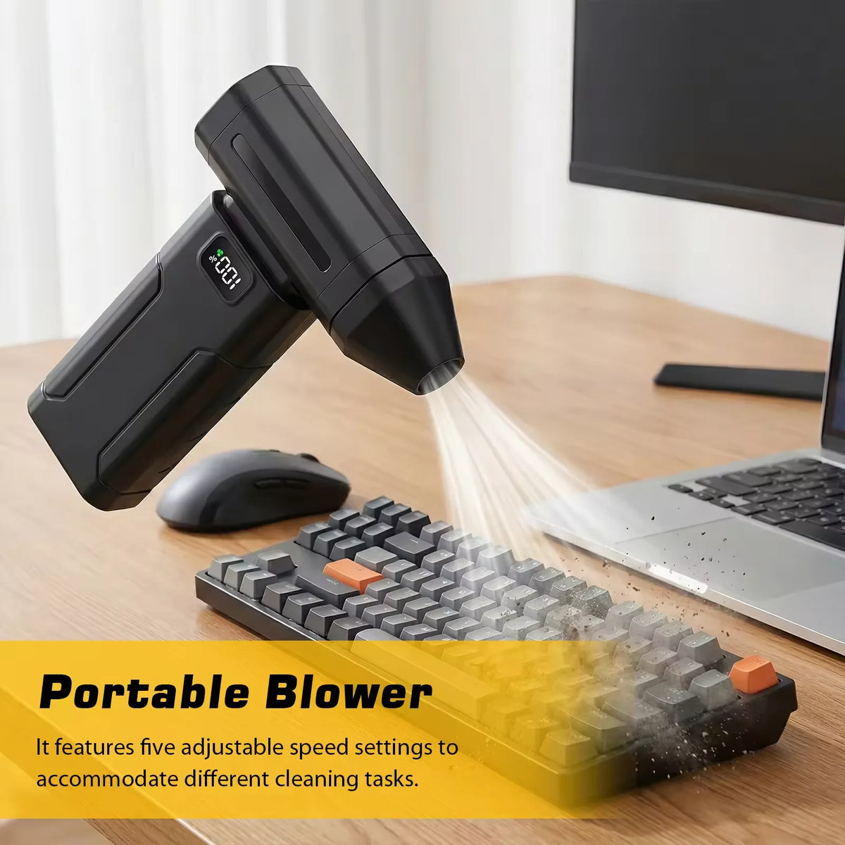 A black portable blower is shown next to a laptop and a textured cleaning brush on a wooden desk.