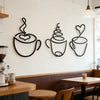 A set of three black iron art coffee cup wall decor pieces displayed on a white wall above a wooden table.