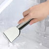 A hand is using a stainless steel multi-purpose scraper to remove ice and snow from a window pane.