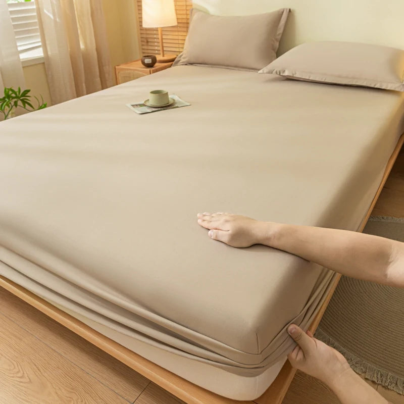 A hand is adjusting a beige fitted sheet on a bed, showing the soft brushed fabric and elastic edge.
