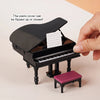 A black 1:12 scale dollhouse piano with a bench is shown, demonstrating that the cover can be flipped up or closed.