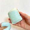 Eine Hand hält einen hellblauen, klebrigen Kartoffel-Stressball-Fidget-Spielzeug vor weißem Hintergrund.