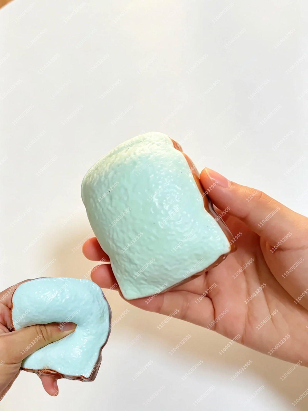 Eine Hand hält einen hellblauen, klebrigen Kartoffel-Stressball-Fidget-Spielzeug vor weißem Hintergrund.