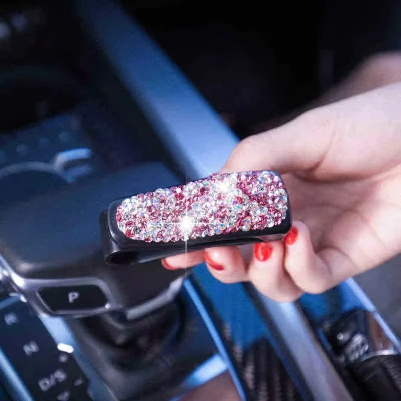 A hand holds a black crystal rhinestone car sun visor sunglasses clip against a dark background.
