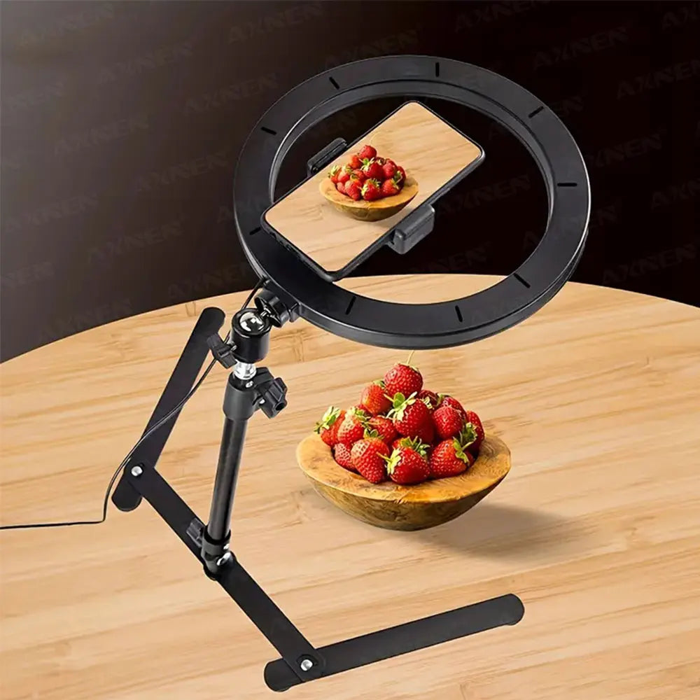 Black foldable overhead tripod with a ring light setup for smartphone photography, positioned above a wooden cutting board wi