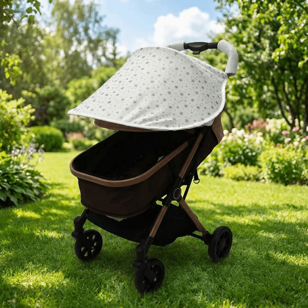 A beige and white stretchable UV-protective stroller sun shade is shown on a black stroller in a sunny outdoor setting.