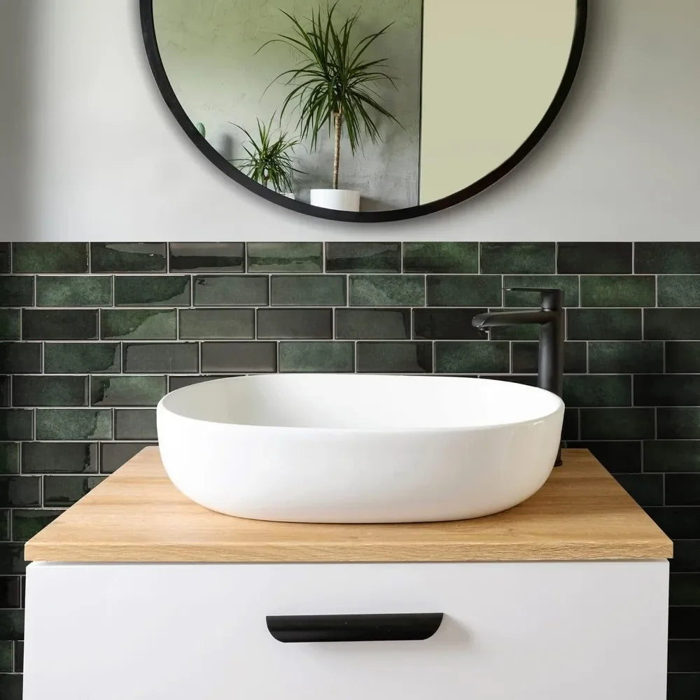 A white vessel sink is displayed on a wooden countertop above a dark subway tile backsplash and a round mirror.