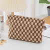 A square makeup bag with a brown and beige checkered pattern resting on a white surface.
