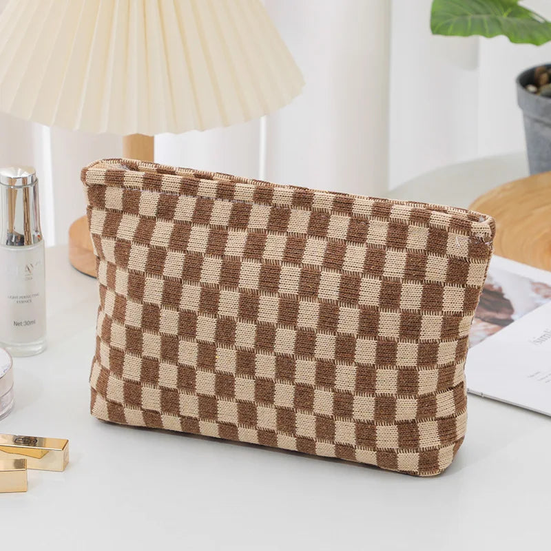 A square makeup bag with a brown and beige checkered pattern resting on a white surface.