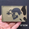 A rectangular tactical patch featuring a silhouette of a skull and crossbones with a camera, made of olive green material.
