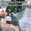 A hand is using a white foam sprayer to apply fine, rich foam onto the surface of a car.