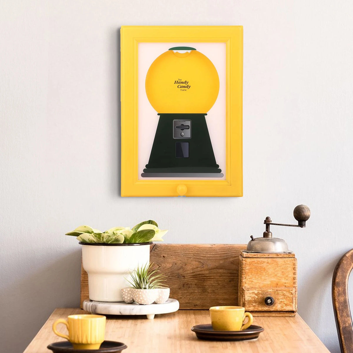 A yellow vintage rotating candy display frame with a dust cover is mounted on a white wall.