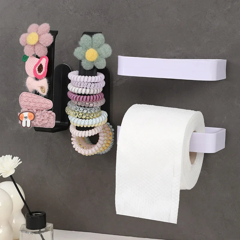 A black wall mount holds a stack of pink and green beaded necklaces and a roll of white toilet paper.