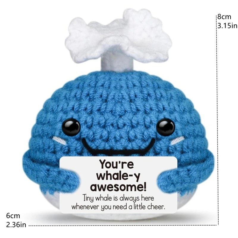 A blue crochet whale doll with a smiling face and a tag that reads You're whale-y awesome!
