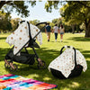 A white breathable stroller cover with sun and dust protection is shown on a stroller in a grassy park setting.