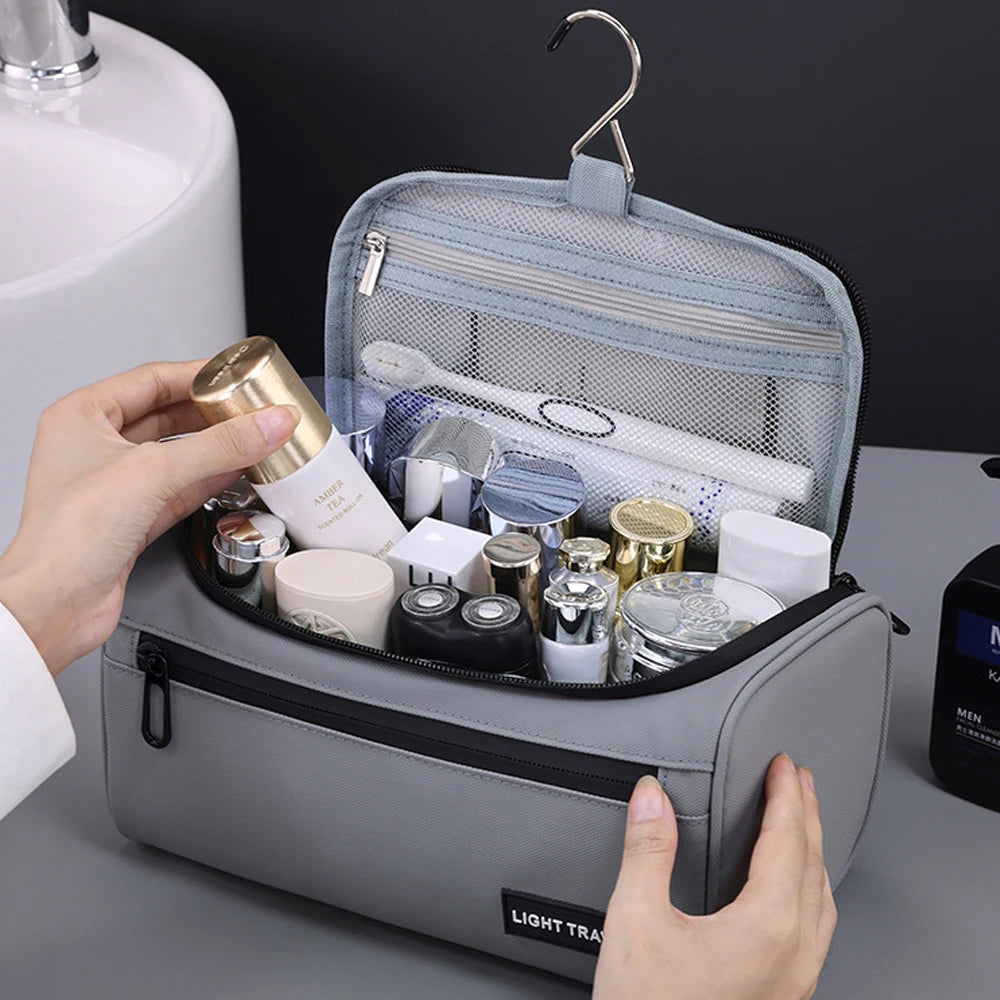 A hand is opening a gray toiletry bag for men, revealing various grooming products inside.