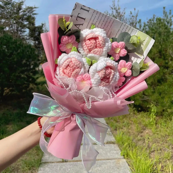 A pink hand-knitted sunflower bouquet with white and pink roses and green foliage.
