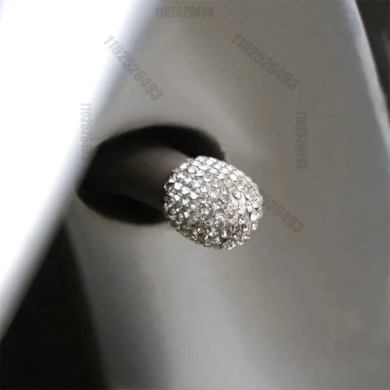 A close-up of a round, brilliant crystal-cut tire valve cap resting on a dark surface.