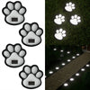 A set of four solar dog paw pathway lights illuminating a stone walkway in a garden.
