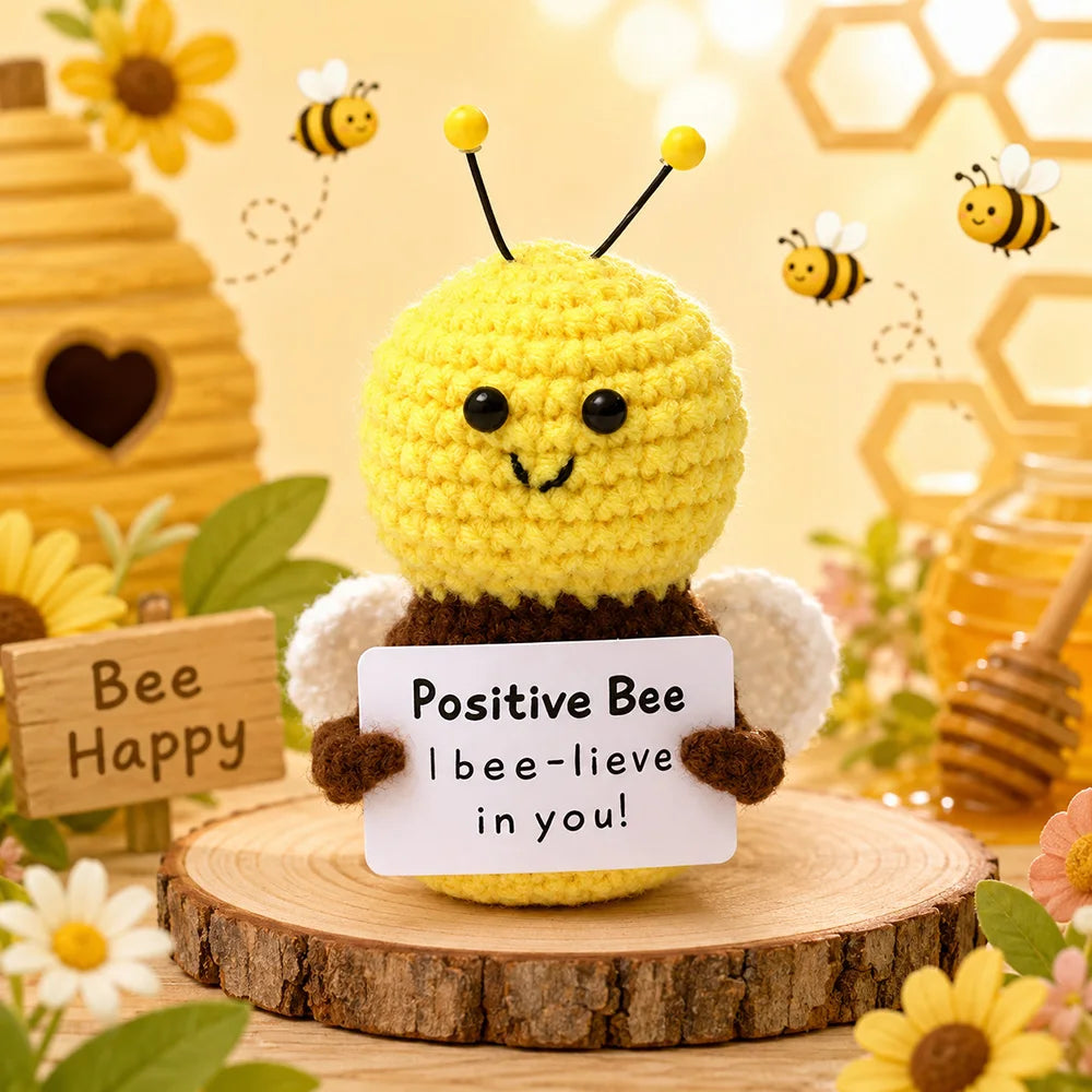 A yellow crochet bee doll with black antennae sits on a wooden slice surrounded by flowers and honeycomb elements.