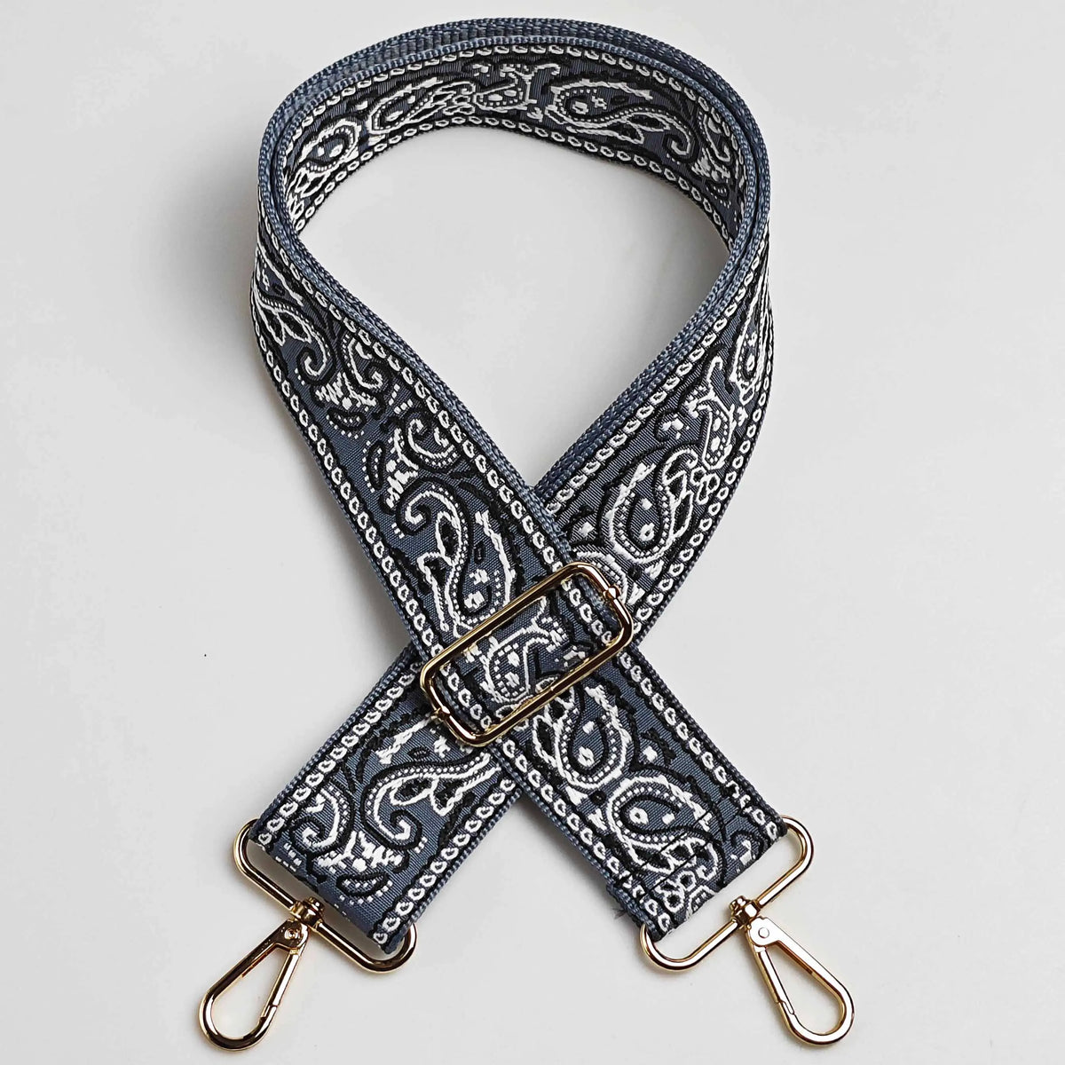 A close-up of a dark blue and white paisley jacquard bag strap with gold hardware.