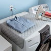 A portable ironing mat is placed on a white ironing board with a shirt and a steam iron nearby.
