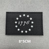 Black fabric patch with white embroidered stars and the year 1776 on a gray background