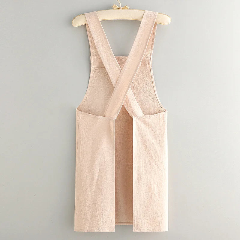 A light beige cotton kitchen apron with adjustable straps hanging on a wooden hanger.
