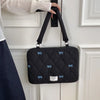 A black quilted laptop shoulder bag with blue bows is hanging on a white door, held by a person's hand.
