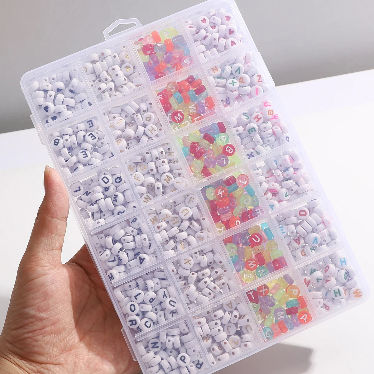 A hand holds an acrylic letter bead set with a grid storage box for jewelry making, showing various colored beads.