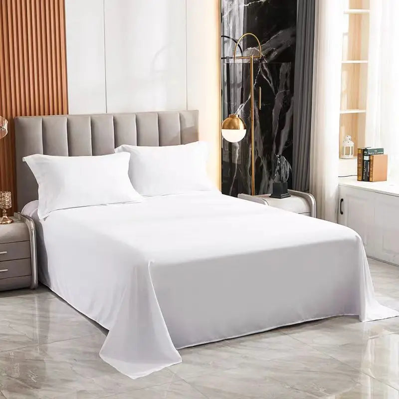 Weiße Premium-Flachbettdecke auf einem Bett mit gepolstertem Kopfteil und dunklen Vorhängen.