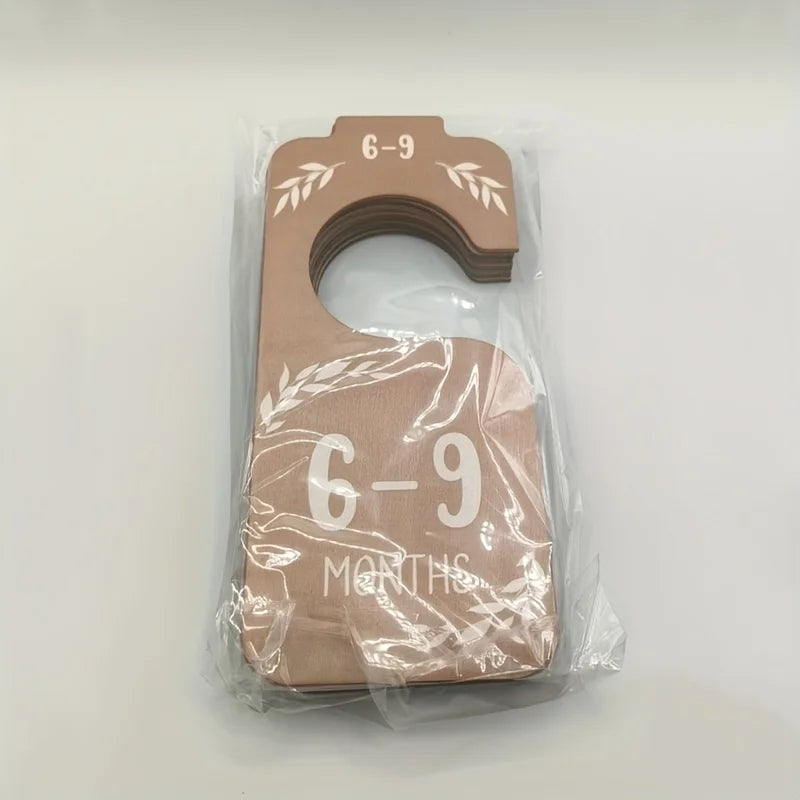 A wooden baby closet divider set with the numbers 6-9 months carved into it, packaged in clear plastic.