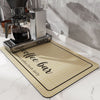 A silver coffee maker and a mat labeled brewed coffee fresh daily are displayed on a white marble surface.