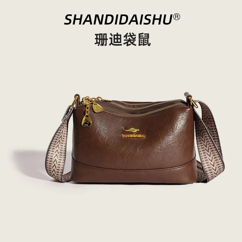 A brown PU leather crossbody shoulder bag with gold hardware and a patterned strap.