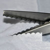 Close-up of professional scalloped pinking shears with sharp blades resting on white fabric.