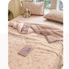 A light pink quilt featuring a cartoon pattern of small animals and flowers, displayed on a bed with a matching pillow.