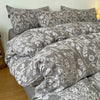 A set of soft printed duvet covers and pillowcases in gray and white floral patterns on a bed.