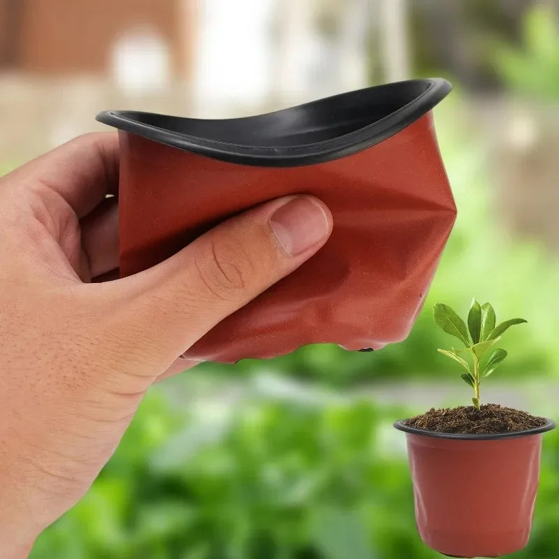 A hand holds a terracotta-colored reusable plastic seedling pot containing a small green plant.
