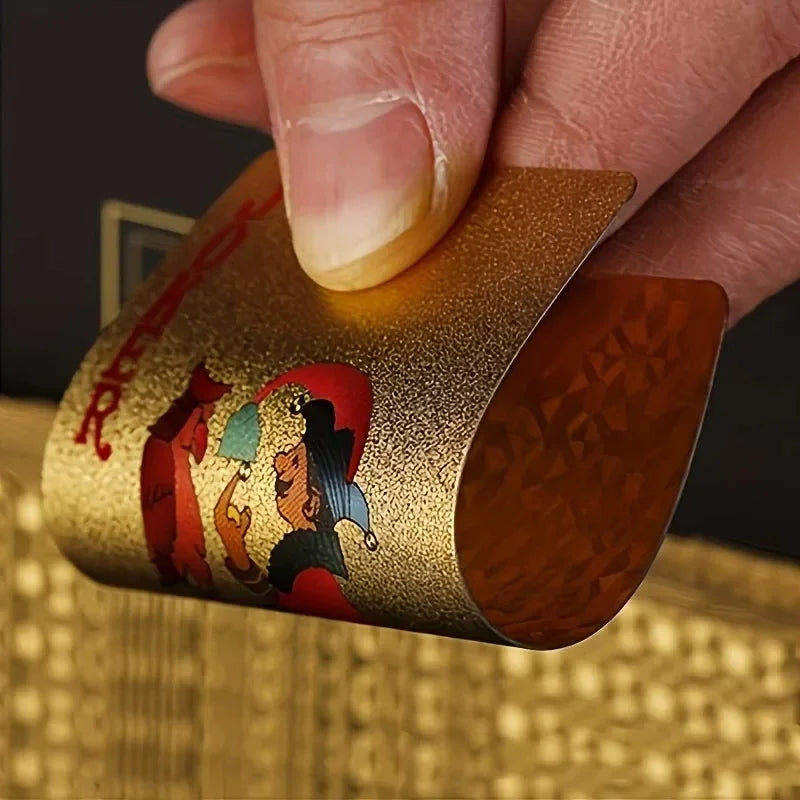 A hand holds a gold foil playing card deck with a matte finish, showing colorful illustrations.
