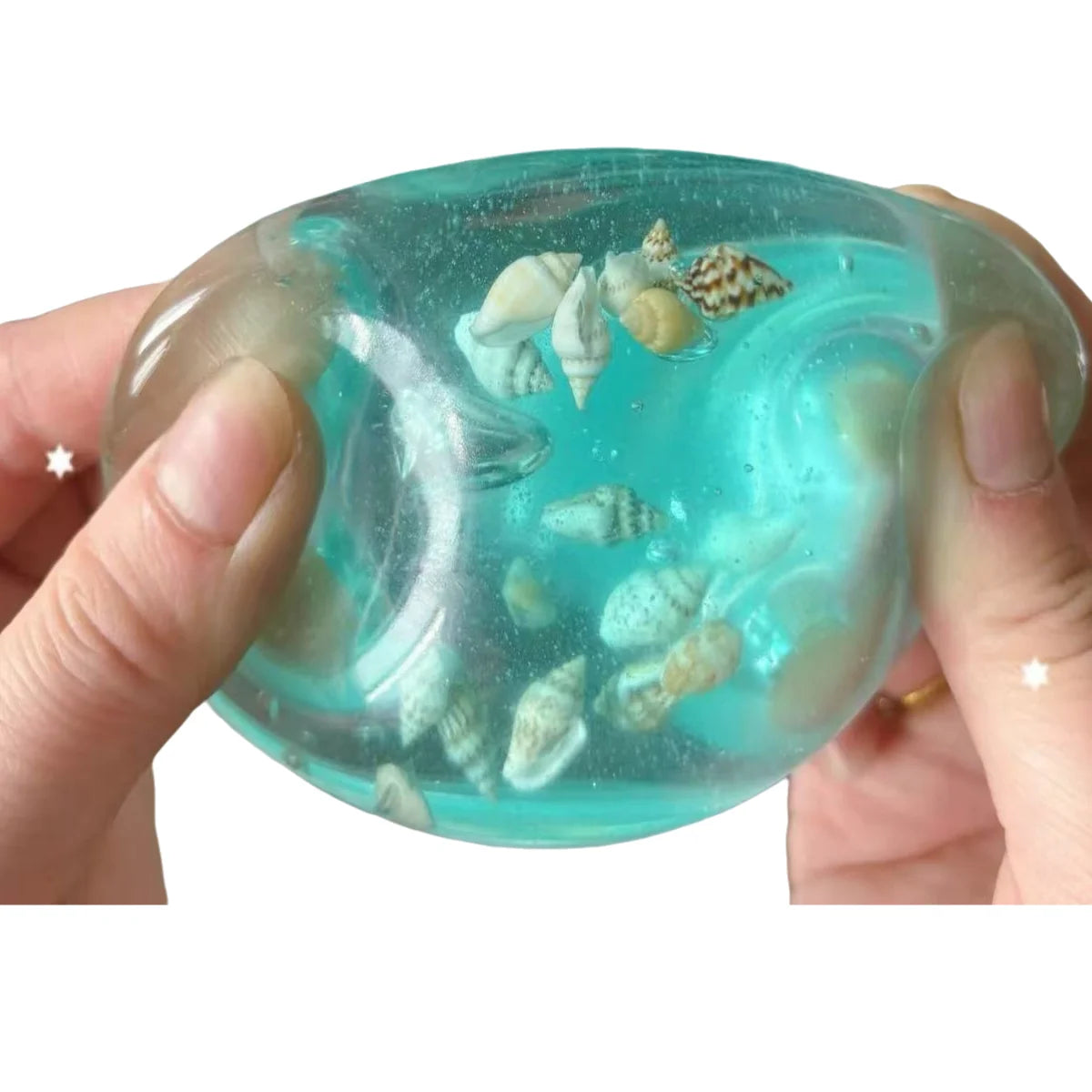 A hand holds a translucent teal squishy stress ball filled with small seashells and sea creatures.