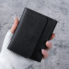 A hand holds a black slim triple-fold PU leather wallet against a gray background.